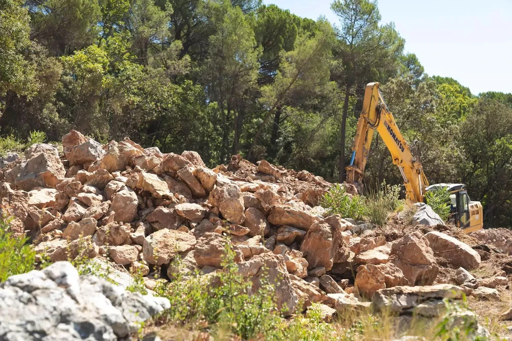 Chantier de construction extérieur avec homme en tenue de travail, casque de sécurité jaune, bras croisés devant bâtiments en construction
